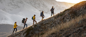 A team of hikers climbs a challenging hill, enwreathed in the glow of a new sunrise.