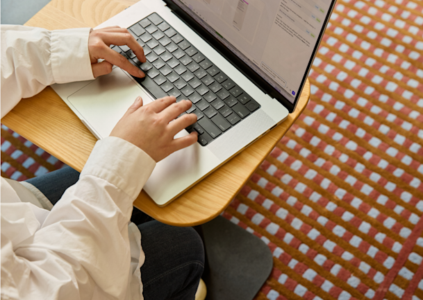 Overhead view of a person typing on a laptop at a small wooden desk.