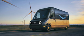 An Amazon delivery truck captured in rolling motion passing a field of wind turbines.